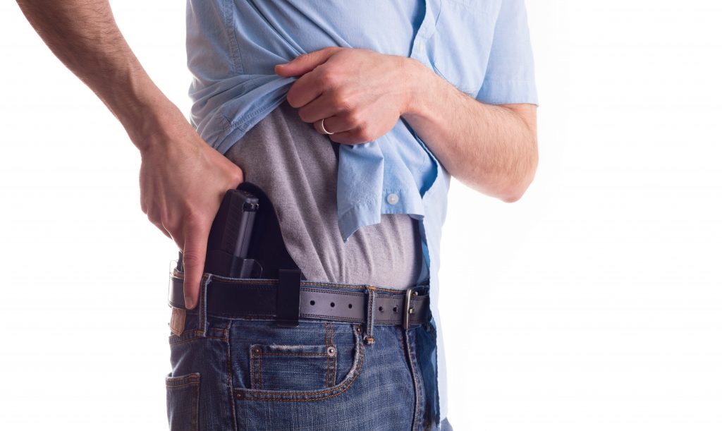 Man lifting shirt pulling his concealed carry pistol from its holster.