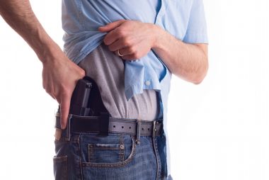 Man lifting shirt pulling his concealed carry pistol from its holster.