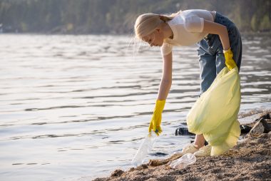 Woman picks up trash at near a lake at summer camp.